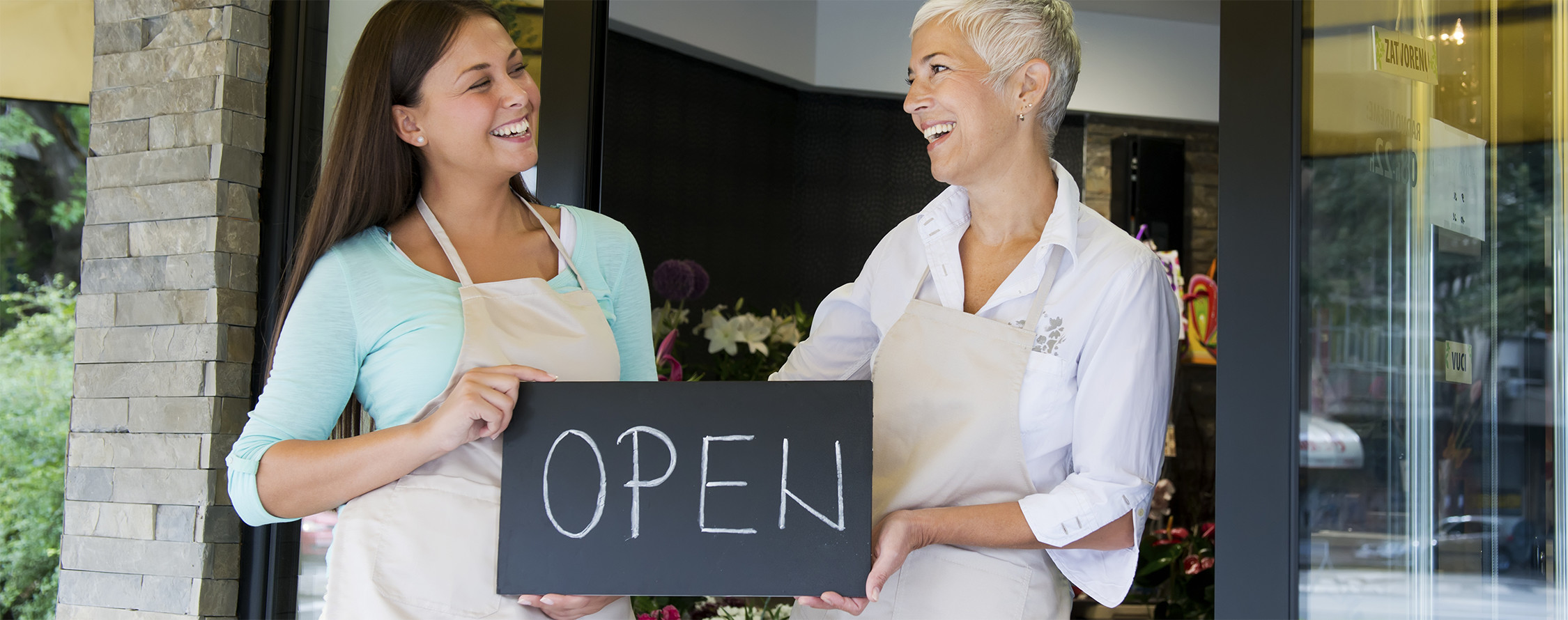 Smiling women in front of store holding open sign